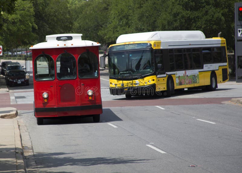 Trolley and city bus heading down the same street on the edge of a downtown area. Trolley and city bus heading down the same street on the edge of a downtown area