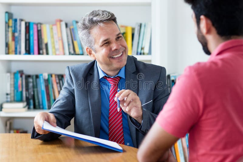 Laughing businessman and applicant signing contract after job interview at office