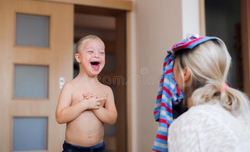 A laughing handicapped down syndrome boy with his mother indoors having fun. royalty free stock photography