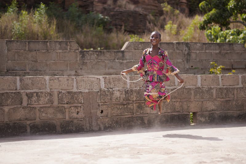 Laughing Little African Girl Tangled In Her Skipping Rope While Playing Outdoor, candid photo of real African children in a natural village environment