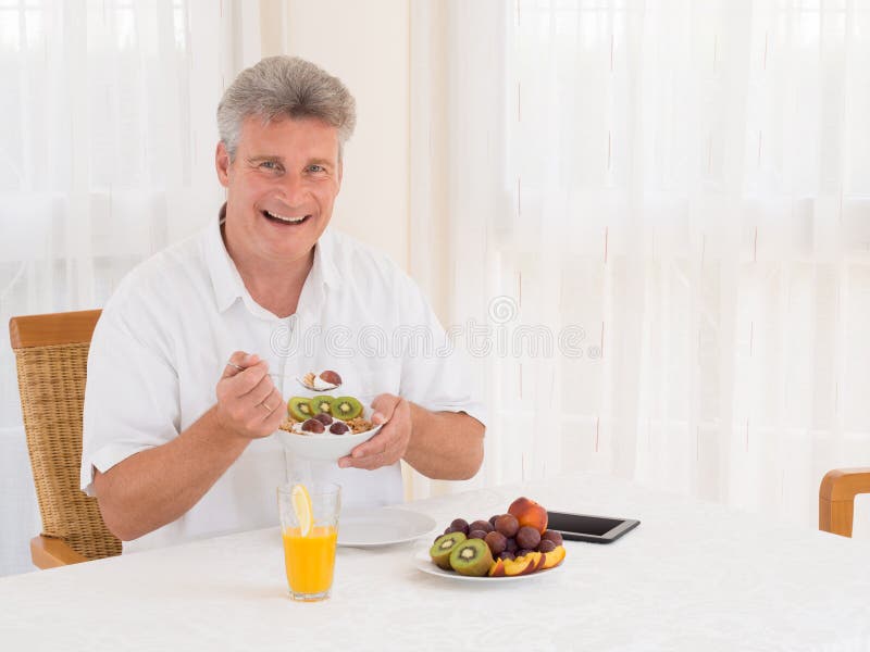Laughing mature man eating a healthy cereal breakfast stock image Laughing mature man eating a healthy cereal breakfast stock image