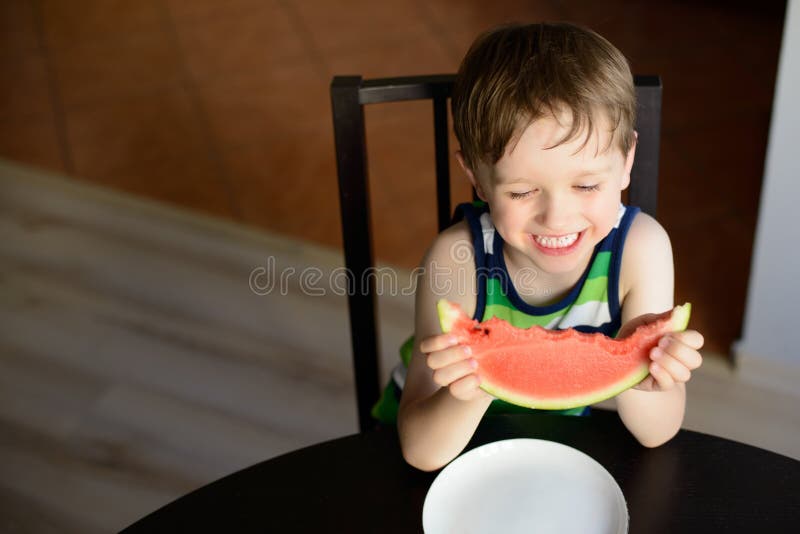 Laughing preschooler eats a watermelon at the table