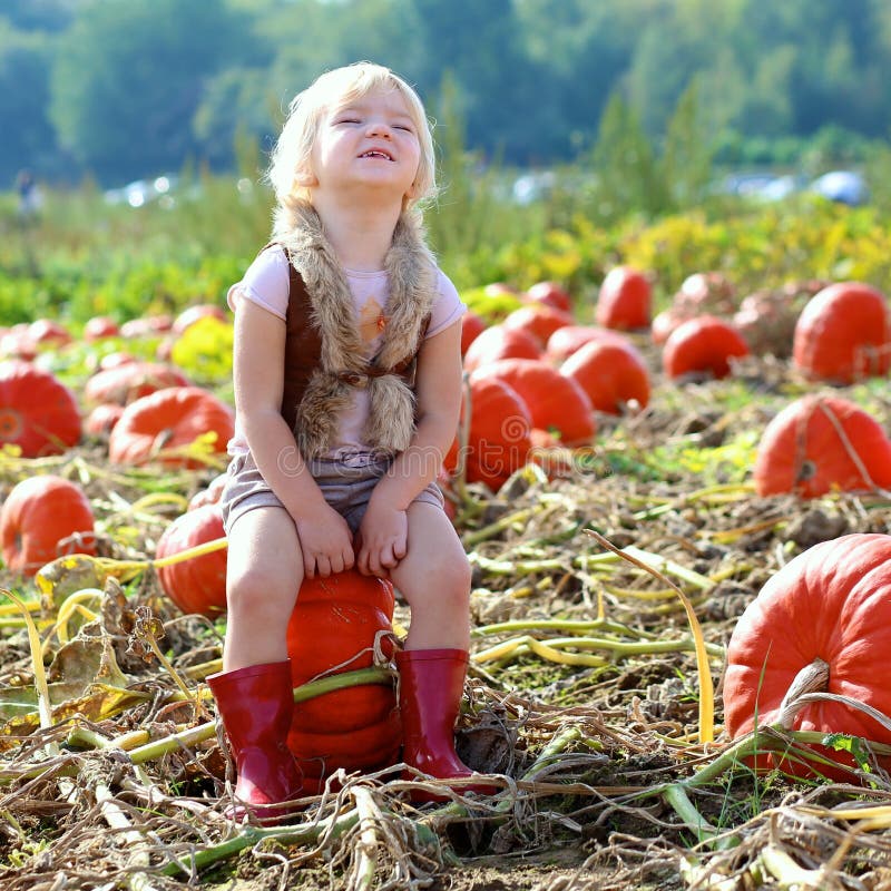 Laughing small girl playing on pumpkin field