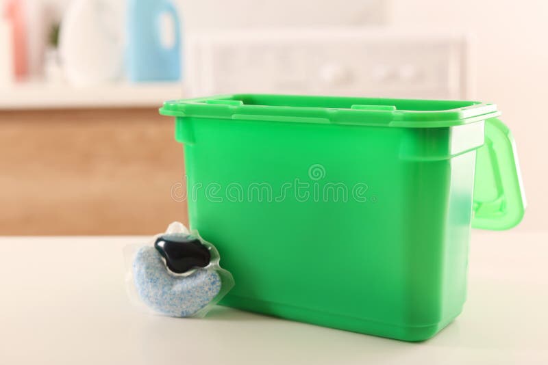 Laundry Container and Washing Detergent Capsule on Table Indoors Stock