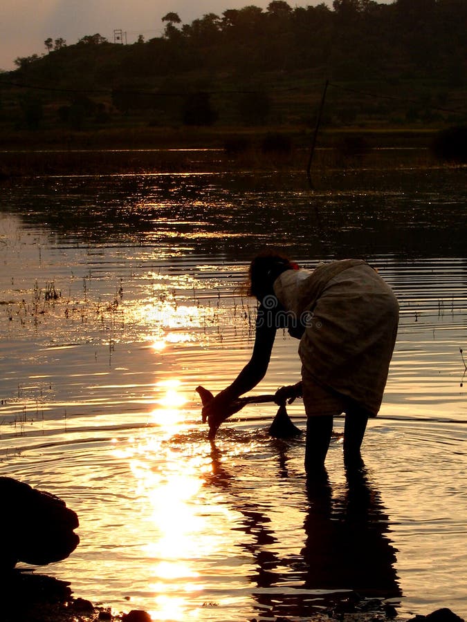 A poor Indian woman washes her clothes in a river at sunset. A poor Indian woman washes her clothes in a river at sunset