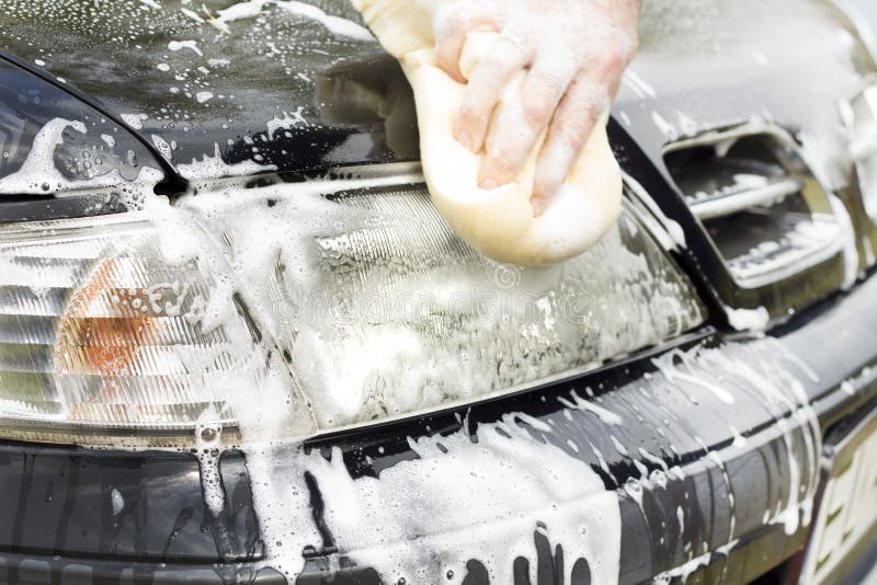 Wash the car headlight with a sponge with plenty of foam. The man`s hand washes the car`s sponge mask with plenty of foam. Wash the car headlight with a sponge with plenty of foam. The man`s hand washes the car`s sponge mask with plenty of foam.