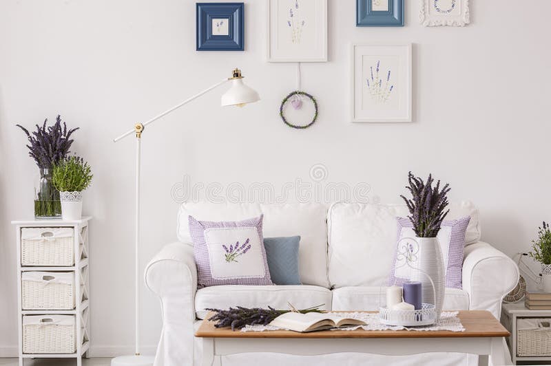 Lavendel blommar på kabinettet bredvid lampan och vitsoffan i vardagsruminre med tabellen och affischer Verkligt foto royaltyfri bild Lavendel blommar på kabinettet bredvid lampan och vitsoffan i vardagsruminre med tabellen och affischer Verkligt foto royaltyfri bild