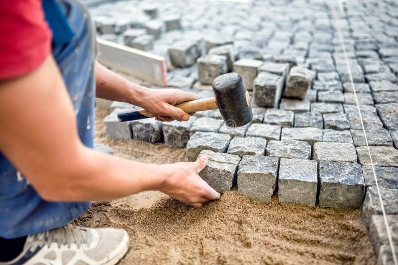 Lavoratore dell'industria che installa i blocchi di pietra sui lavori di costruzione della pavimentazione, della via o del marcia fotografia stock libera da diritti Lavoratore dell'industria che installa i blocchi di pietra sui lavori di costruzione della pavimentazione, della via o del marcia fotografia stock libera da diritti
