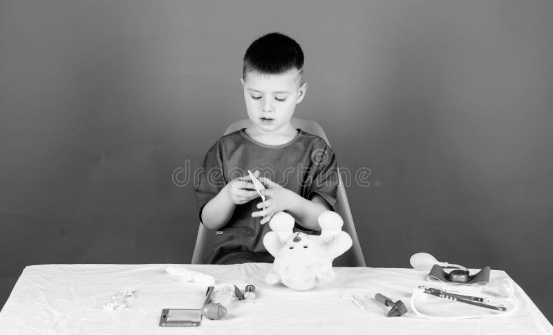 Lavoratore dell'ospedale Ritardi e braccia Piccolo medico del bambino occupato si siede la tavola con gli strumenti medici Esame fotografie stock libere da diritti Lavoratore dell'ospedale Ritardi e braccia Piccolo medico del bambino occupato si siede la tavola con gli strumenti medici Esame fotografie stock libere da diritti
