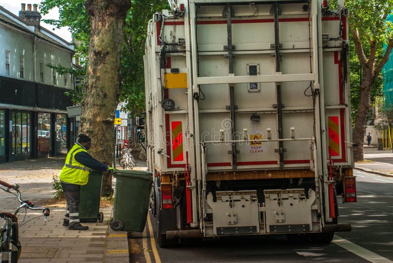 Lavoratore dello spreco e del bidone della spazzatura di riciclaggio municipali urbani di caricamento del camion del collettore d immagine stock libera da diritti Lavoratore dello spreco e del bidone della spazzatura di riciclaggio municipali urbani di caricamento del camion del collettore d immagine stock libera da diritti