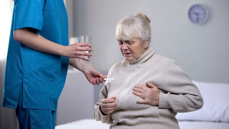 Lavoratore medico che d? a pillole signora anziana che soffre dal dolore del cuore, trattamento fotografie stock Lavoratore medico che d? a pillole signora anziana che soffre dal dolore del cuore, trattamento fotografie stock