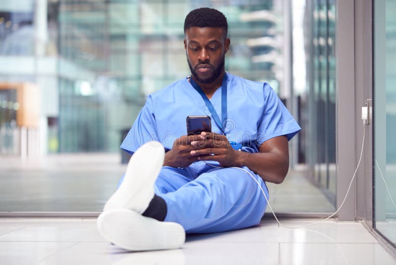 Male Medical Worker In Hospital Addicted To Using Mobile Phone At Work. Male Medical Worker In Hospital Addicted To Using Mobile Phone At Work