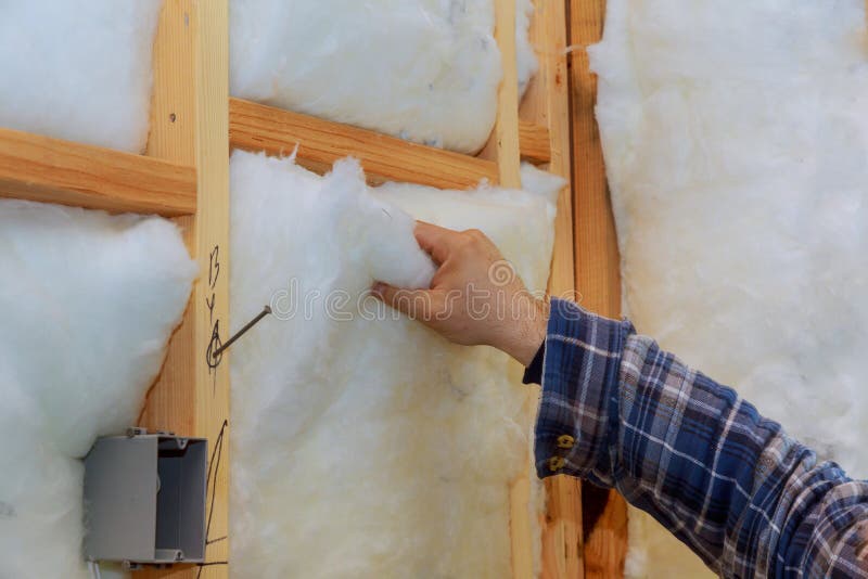 Lavoratore nell'isolamento d'isolamento della lana di roccia nel telaio di legno per le pareti future della casa per la casa cald immagini stock Lavoratore nell'isolamento d'isolamento della lana di roccia nel telaio di legno per le pareti future della casa per la casa cald immagini stock