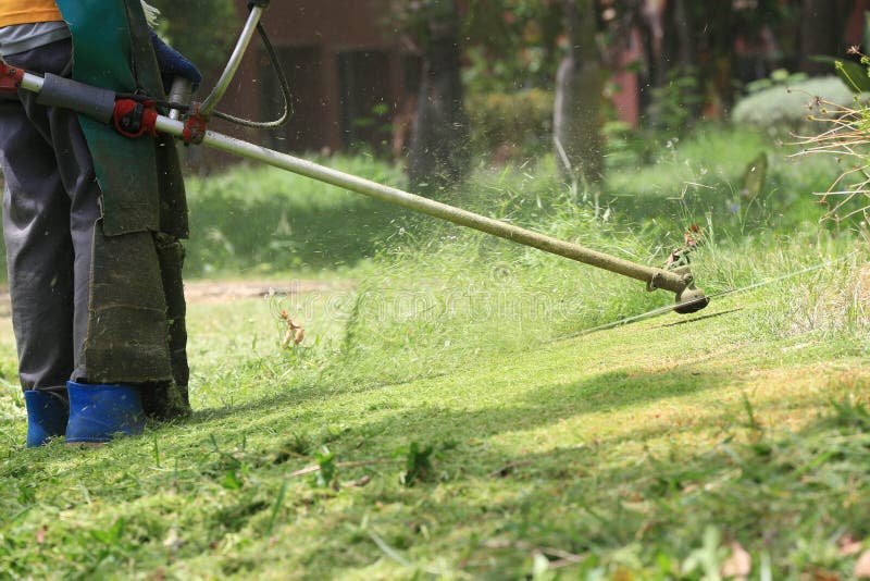 Lawn mower worker cutting grass in green field stock image
