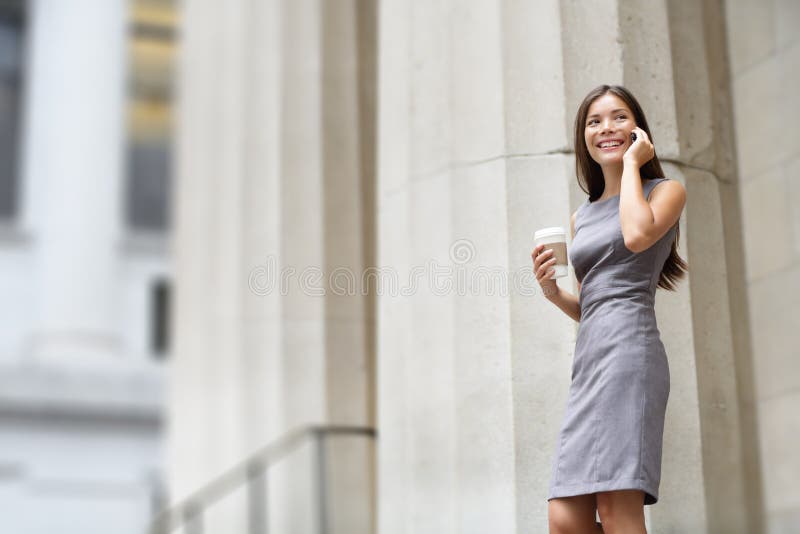 Lawyer businesswoman professional walking outdoors talking on cell smart phone drinking coffee from disposable paper cup. Multiracial Asian / Caucasian businesswoman smiling