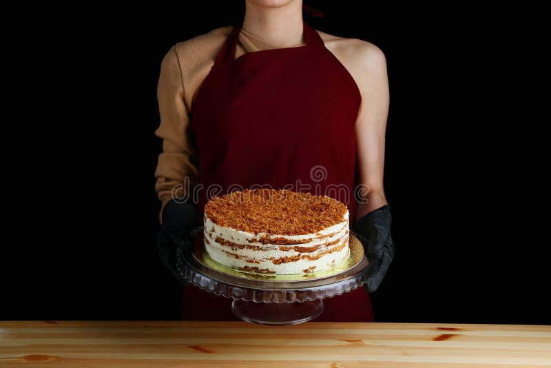 Layered honey cake on a wooden table. woman confectioner hold honney dessert cake on black isolated background. gloved hands of a