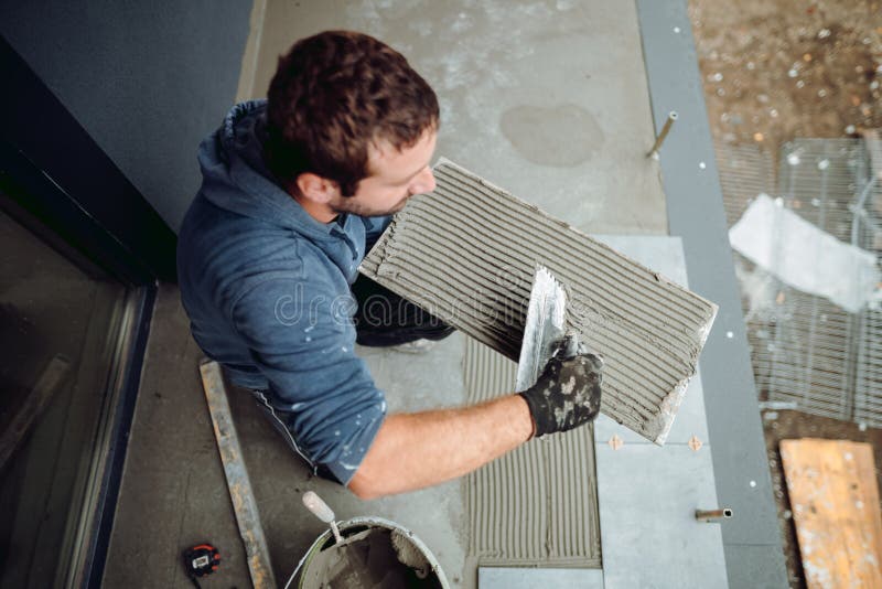 Worker Placing Ceramic Floor Tile in Position Over Adhesive Stock Photo