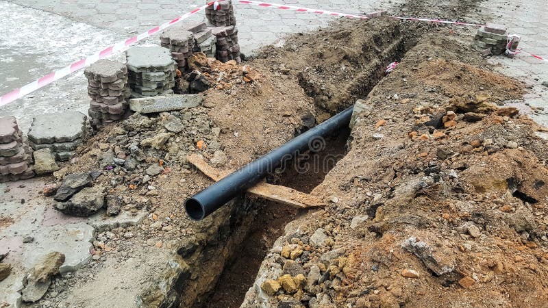 Laying installation of a new cable in a plastic pipe. Digging drilling of the earth for pipe replacement, sewer. Work with drainage royalty free stock photo