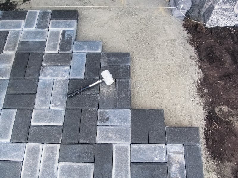 Laying paving brick slabs on a dry cement-sand mix, top view. Rubber mallet lies on the surface of gray paving stones, beautiful stock images