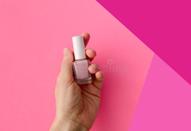 Layout of a glass bottle in the hands of a woman. Pink colored container with nail polish. Beauty concept