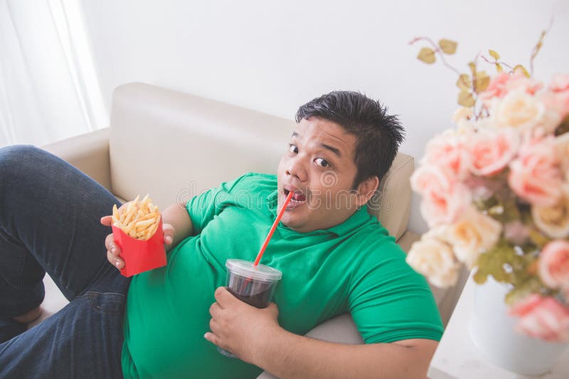 Lazy obese person eats junk food while laying on a couch