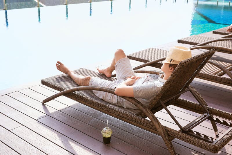 Lazy time. Asian guy sleeping on the couch swimming pool in summer royalty free stock photography