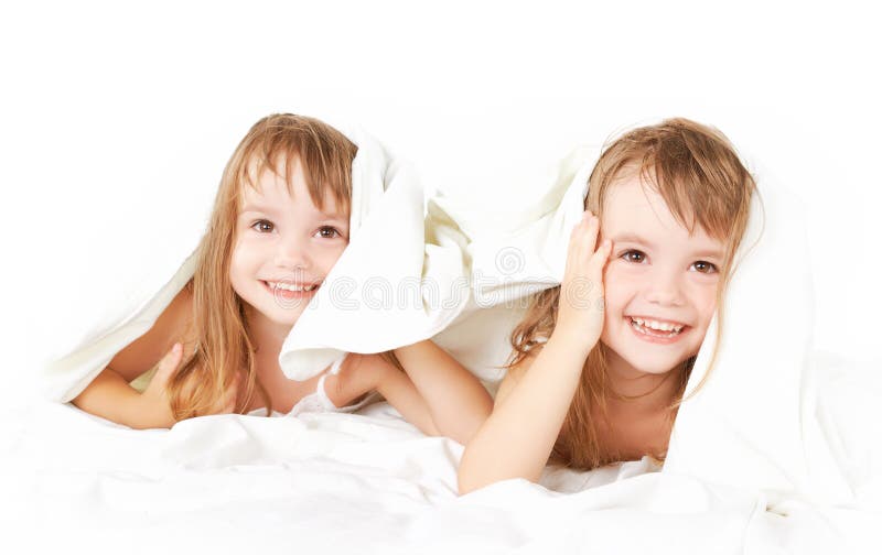 Le bambine felici gemella la sorella a letto nell'ambito del divertiresi generale fotografia stock Le bambine felici gemella la sorella a letto nell'ambito del divertiresi generale fotografia stock