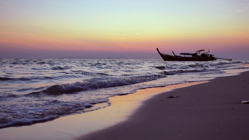 Le bateau de pêche de silhouette se balançant en mer avec la vague de mer lavage mousses sur le fond tropical de plage de sable da