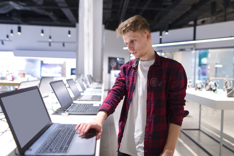 Le beau jeune acheteur choisit un ordinateur portable dans un magasin moderne de l'électronique images stock