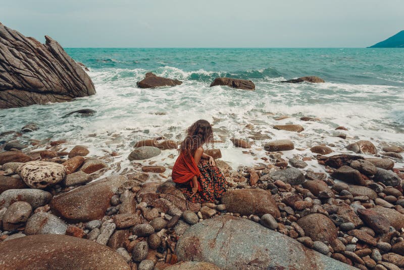 Le beau jeune boho a dénommé la femme s'asseyant sur une plage en pierre