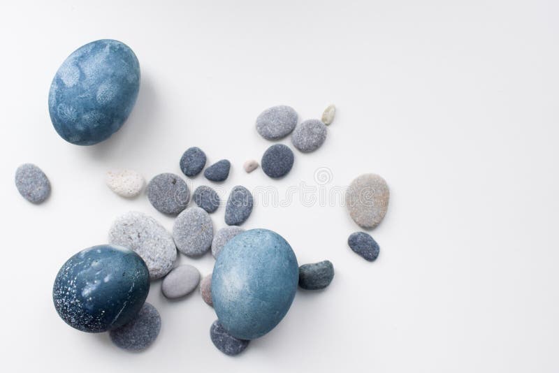 Le bleu coloré par trois, les oeufs de marbre gris se trouvent sur un fond blanc parmi les pierres photo libre de droits Le bleu coloré par trois, les oeufs de marbre gris se trouvent sur un fond blanc parmi les pierres photo libre de droits