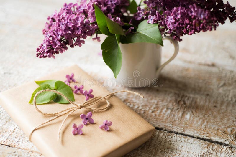 Le bouquet lilas pourpre dans le vase et le présent s'est étendu sur la table en bois photographie stock Le bouquet lilas pourpre dans le vase et le présent s'est étendu sur la table en bois photographie stock