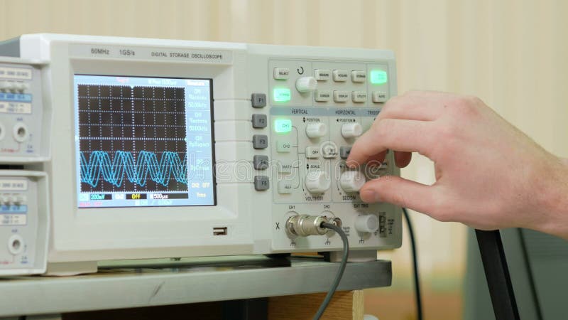 Le bras d'ingénierie du ` s d'hommes ajuste l'oscilloscope à l'affichage approprié du signal électrique Petit industriel moderne