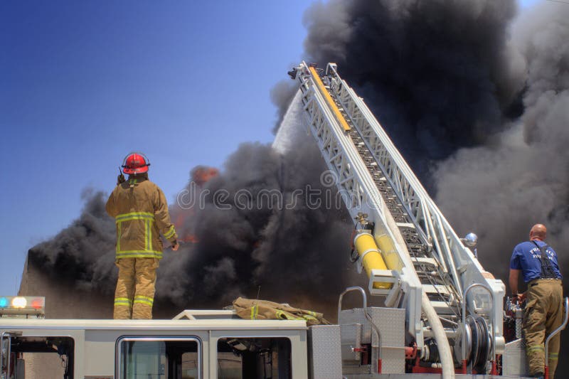 Fireman on a ladder truck direct a stream of water onto a burning building. Fireman on a ladder truck direct a stream of water onto a burning building