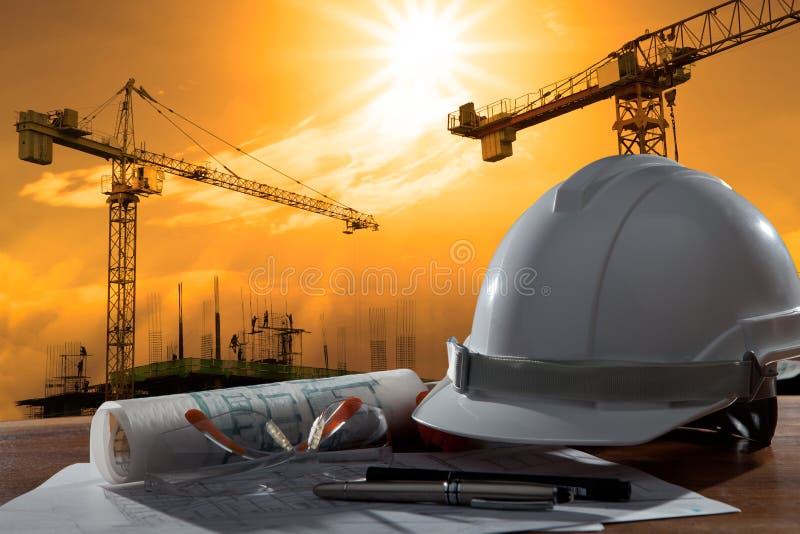 File of safety helmet and architect pland on wood table with sunset scene and building construction. File of safety helmet and architect pland on wood table with sunset scene and building construction