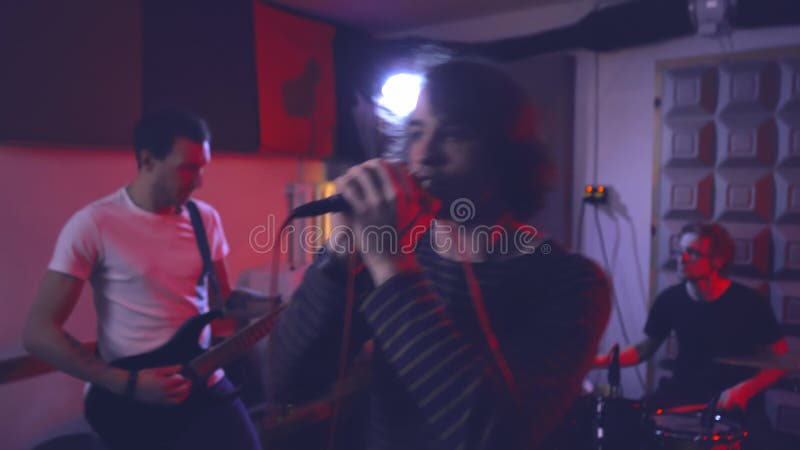Le chanteur chante une chanson dans le microphone accompagnée de guitare et de batterie. banque de vidéos