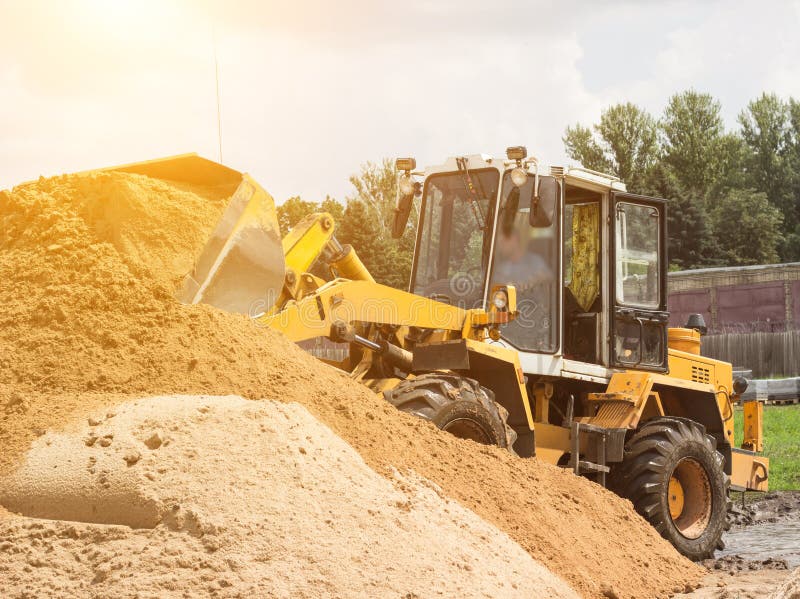 Le chargeur jaune de tracteur prend un seau de la terre, mécanique, de poche avec la terre et de soleil images libres de droits Le chargeur jaune de tracteur prend un seau de la terre, mécanique, de poche avec la terre et de soleil images libres de droits