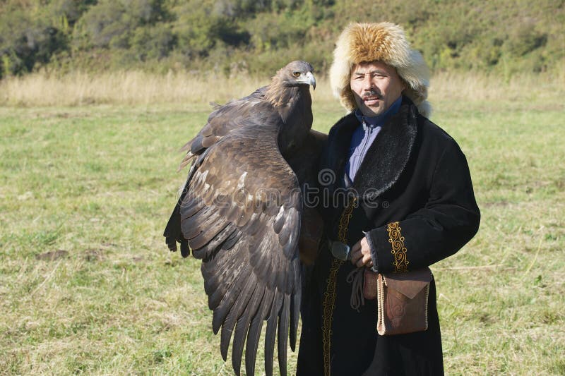 Le chasseur mongol dans la robe traditionnelle tient l'aigle d'or vers Almaty, Kazakhstan photographie stock Le chasseur mongol dans la robe traditionnelle tient l'aigle d'or vers Almaty, Kazakhstan photographie stock