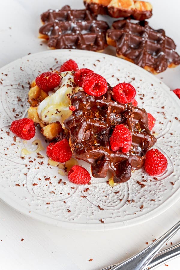 Le chocolat belge waffles avec les framboises fraîches, la crème fouettée et le sirop de miel photographie stock libre de droits Le chocolat belge waffles avec les framboises fraîches, la crème fouettée et le sirop de miel photographie stock libre de droits
