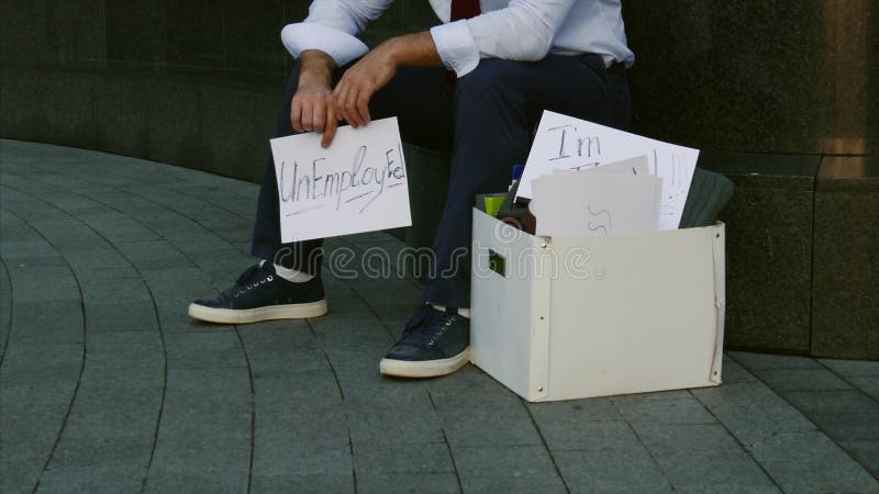 Le chômage, chômeur, renvoi, réduction de taille Un homme sans travail Un jeune homme s'assied sur la rue avec un signe banque de vidéos