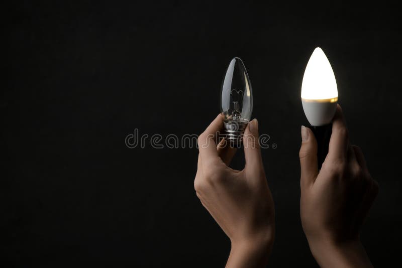 Le concept de l'électricité d'économie Ampoules dans des mains sur un fond noir le choix entre une lumière simple et économique image stock Le concept de l'électricité d'économie Ampoules dans des mains sur un fond noir le choix entre une lumière simple et économique image stock