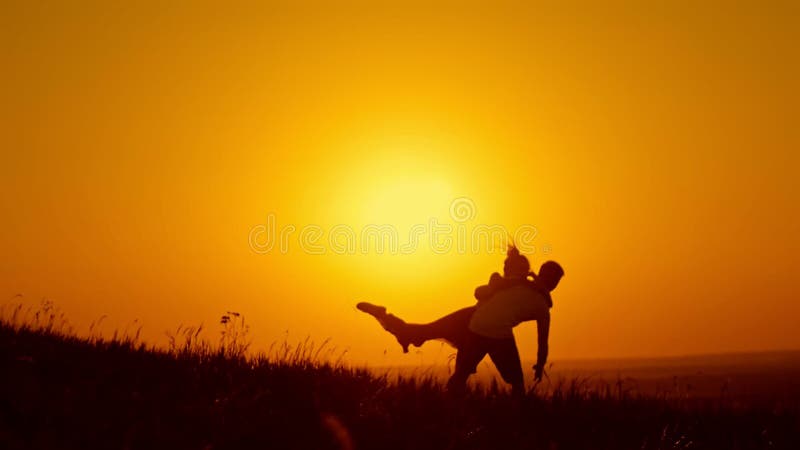 Le coppie amorose - il giovane e bello dancing della ragazza sul prato dell'estate al tramonto ed hanno gli abbracci e bacio, sil