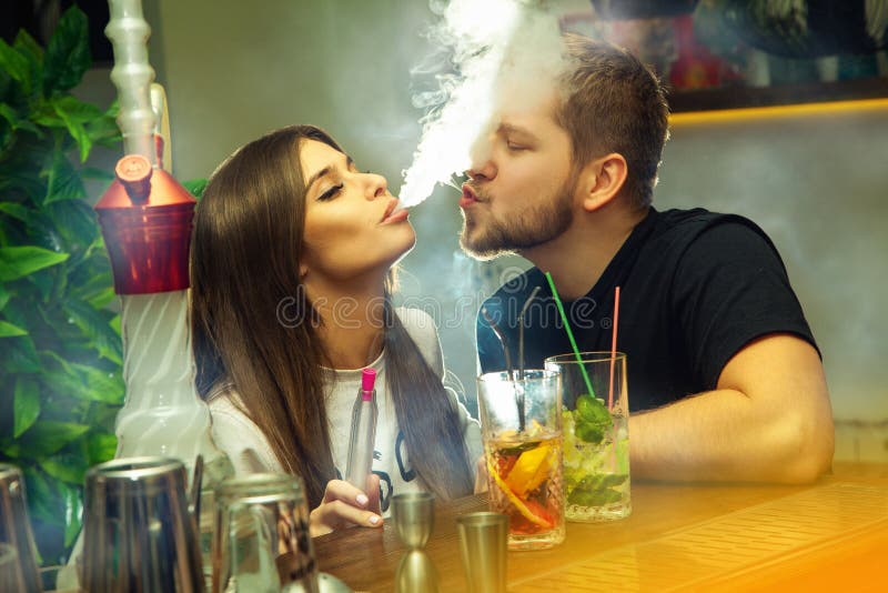 Beautiful couple in love smokes hookah and drinks cocktails in the bar. Beautiful couple in love smokes hookah and drinks cocktails in the bar