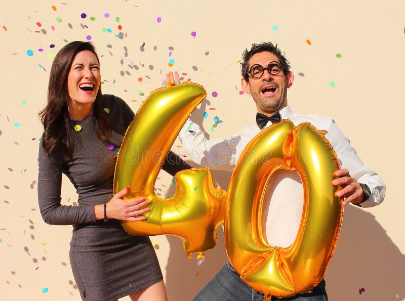 Le couple gai célèbre un anniversaire de quarante ans avec de grands ballons d'or et petits morceaux de papier colorés dans le ci photo stock Le couple gai célèbre un anniversaire de quarante ans avec de grands ballons d'or et petits morceaux de papier colorés dans le ci photo stock