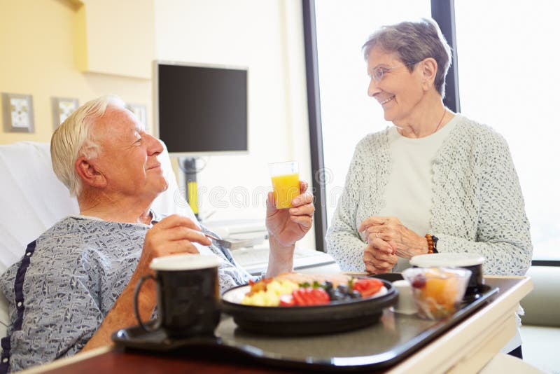 Le couple supérieur dans la chambre d'hôpital en tant que patient masculin prend le déjeuner images stock Le couple supérieur dans la chambre d'hôpital en tant que patient masculin prend le déjeuner images stock