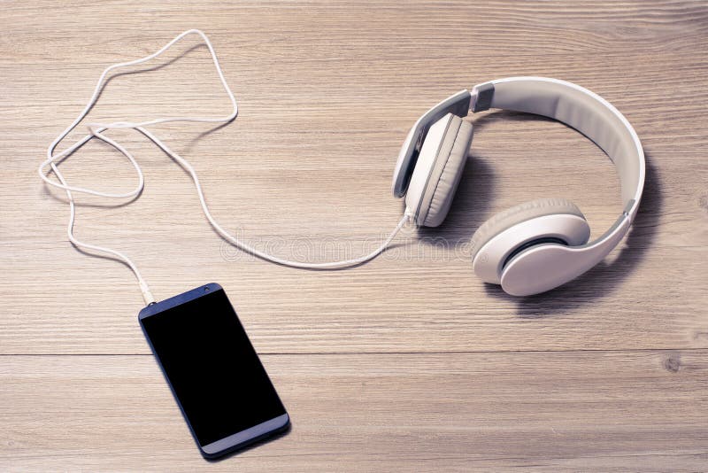 Le cuffie ed il telefono cellulare bianchi su una musica di tavola ascoltano cuffie dell'amante il resto di tempo libero che di h fotografie stock Le cuffie ed il telefono cellulare bianchi su una musica di tavola ascoltano cuffie dell'amante il resto di tempo libero che di h fotografie stock