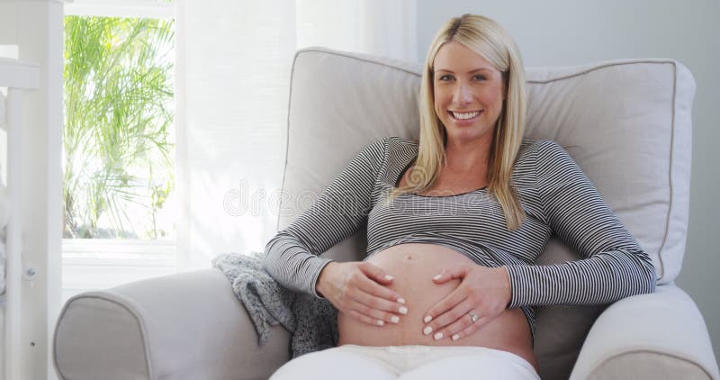 Le den le och gnidande buken för gravid kvinna i barnkammare arkivbild Le den le och gnidande buken för gravid kvinna i barnkammare arkivbild