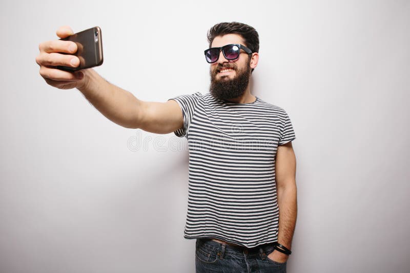 Le den lyckliga hipstermannen i solexponeringsglas med skägget som tar selfie med mobiltelefonen royaltyfri bild Le den lyckliga hipstermannen i solexponeringsglas med skägget som tar selfie med mobiltelefonen royaltyfri bild
