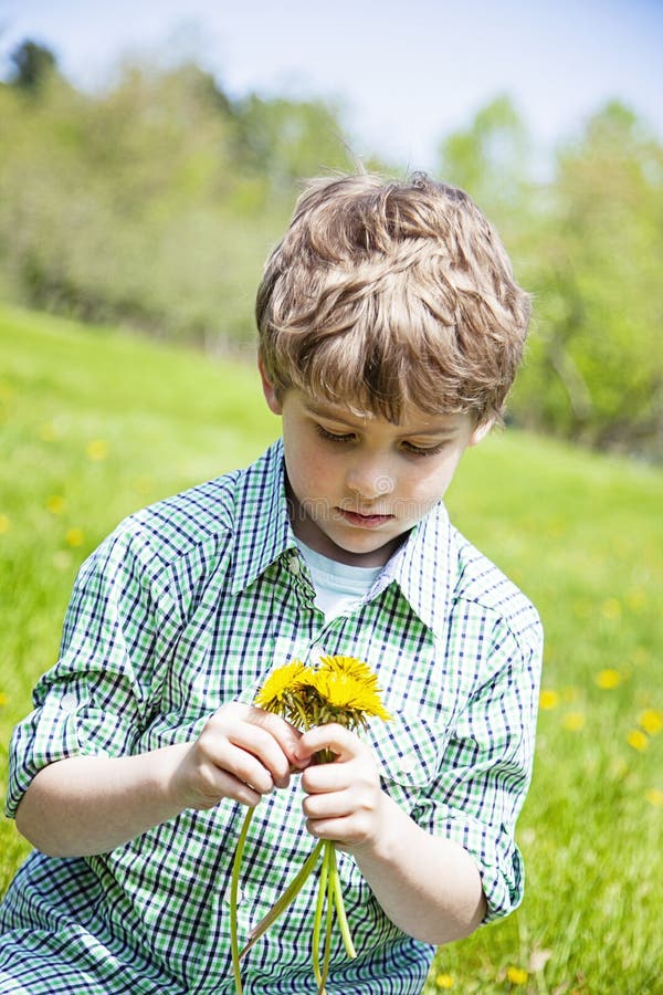 Le den lyckliga pojken som sitter i gräs utanför val av blommor fotografering för bildbyråer