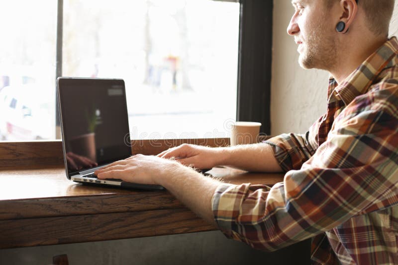 Le den skäggiga affärsmannen som bär tillfälliga hipsterkläder genom att använda bärbar dator- och cellsmartphonen i coffehus royaltyfri foto Le den skäggiga affärsmannen som bär tillfälliga hipsterkläder genom att använda bärbar dator- och cellsmartphonen i coffehus royaltyfri foto